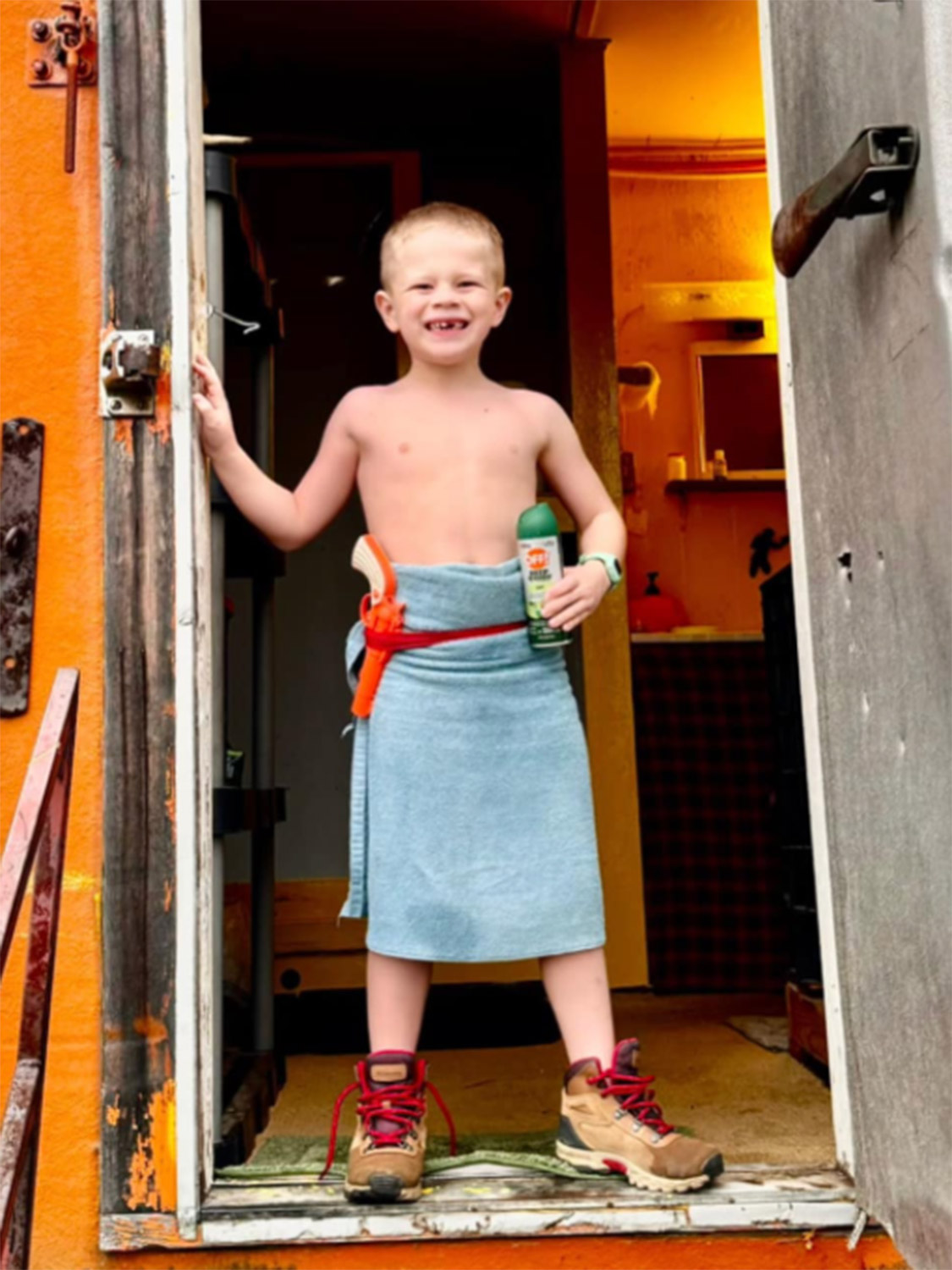 Knox After the Best Shower of His Life – Kavik River Camp Alaska Kids Knox Neumayr standing in the doorway of the Kavik River Camp bathhouse wrapped in a towel with a Nerf gun holster and bug spray, grinning after a shower on Alaska's North Slope