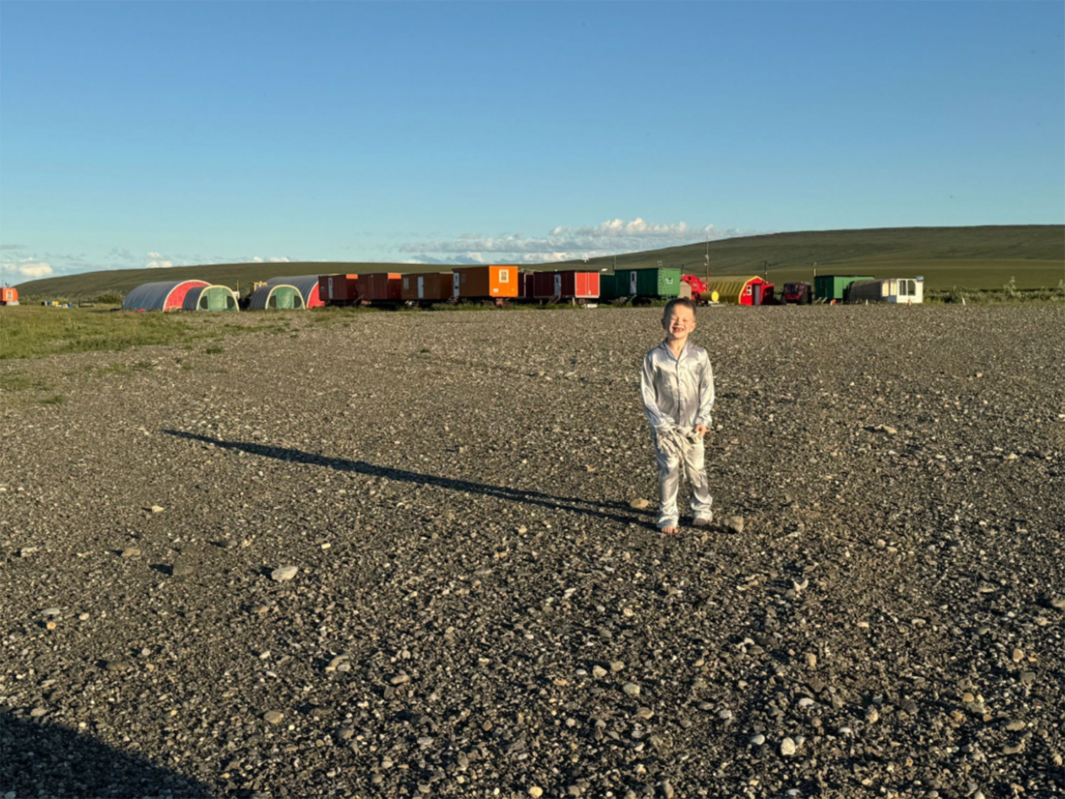 Midnight Sun at Kavik River Camp – Arctic Alaska Summer Light Knox Neumayr standing on the gravel airstrip at Kavik River Camp at midnight under the Arctic summer sun, with the camp's colorful sleeping trailers visible behind him on Alaska's North Slope
